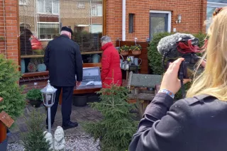 Een cameravrouw filmt twee mensen die voor een raam staan